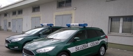 Zdjęcie przedstawia dwa oznakowane radiowozy marki ford Focus ustawione na placu w Izbie Administracji Skarbowej w Olsztynie