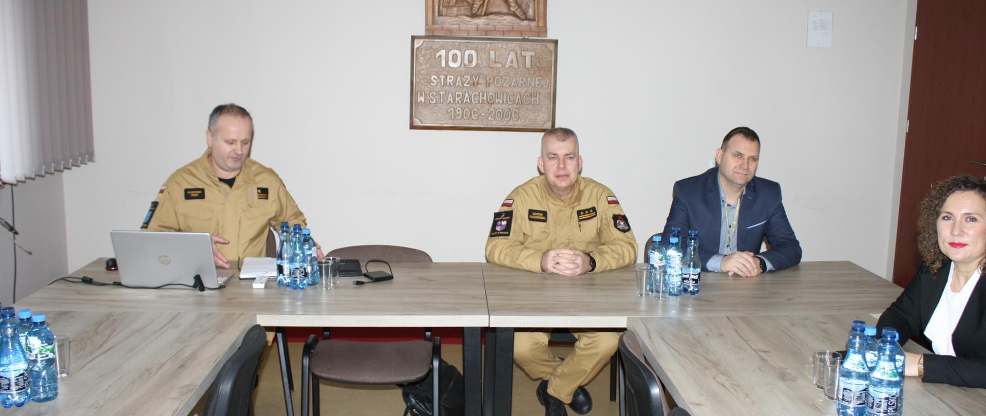 Zaproszeni goście siedzący przy stole na naradzie rocznej, przemawia stojąc Komendant Powiatowy PSP w Starachowicach mł. bryg. Sławomir Zięba