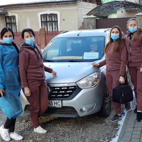 Cztery kobiety w maseczkach stoją obok samochodu.
