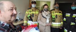 Zdjęcie przedstawia 4 strażaków i pracownika cywilnego KPPSP w Tucholi w mieszkaniu, do którego dostarczono prezenty w ramach akcji „Świąteczna Tucholska Paczka” organizowanej przez Miejski Ośrodek Pomocy Społecznej w Tucholi. Na pierwszym planie zdjęcia widać Pana Krzysztofa i prezenty, które otrzymał. 