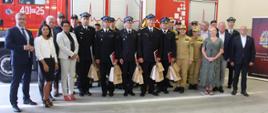 Zdjęcie przedstawia strażaków i samorządowców podczas uroczystej zmiany służby.
W tle garaż JRG i samochody strażackie.
