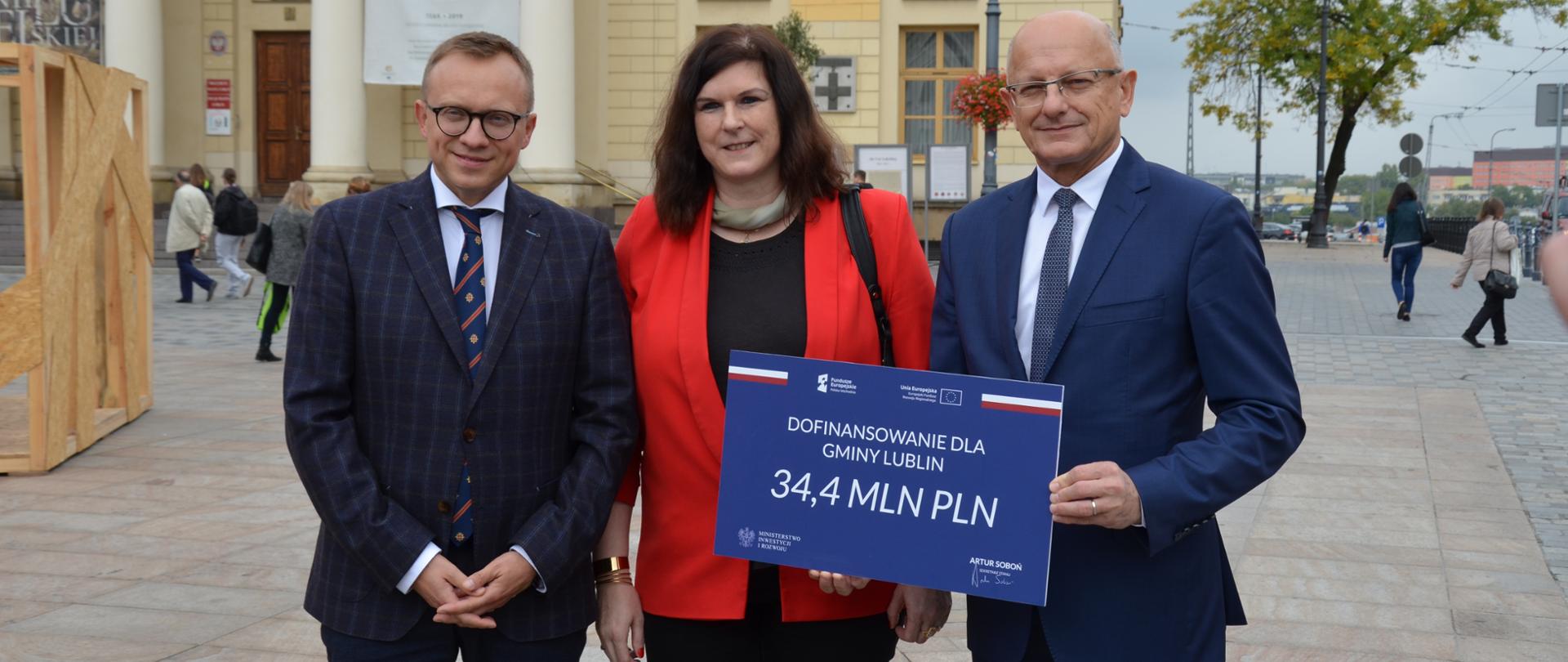 Minister Soboń wraz z dwoma innymi osobami stoi z banerem na którym jest napisane Dofinansowanie dla Gminy Lublin, 34,4 mln zł