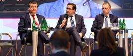 Wiceminister rozwoju i technologii Mariusz Jerzy Golecki przemawiający przez mikrofon w trakcie dyskusji panelowe poświęconej wzmacnianiu inwestycji w Polsce podczas konferencji Europejskiego Banku Inwestycyjnego, po lewej od ministra Goleckiego siedzi prezes zarządu Banku Pekao SA Leszek Skiba, zaś po prawej członek zarządu Banku Gospodarstwa Krajowego Tomasz Robaczyński.
