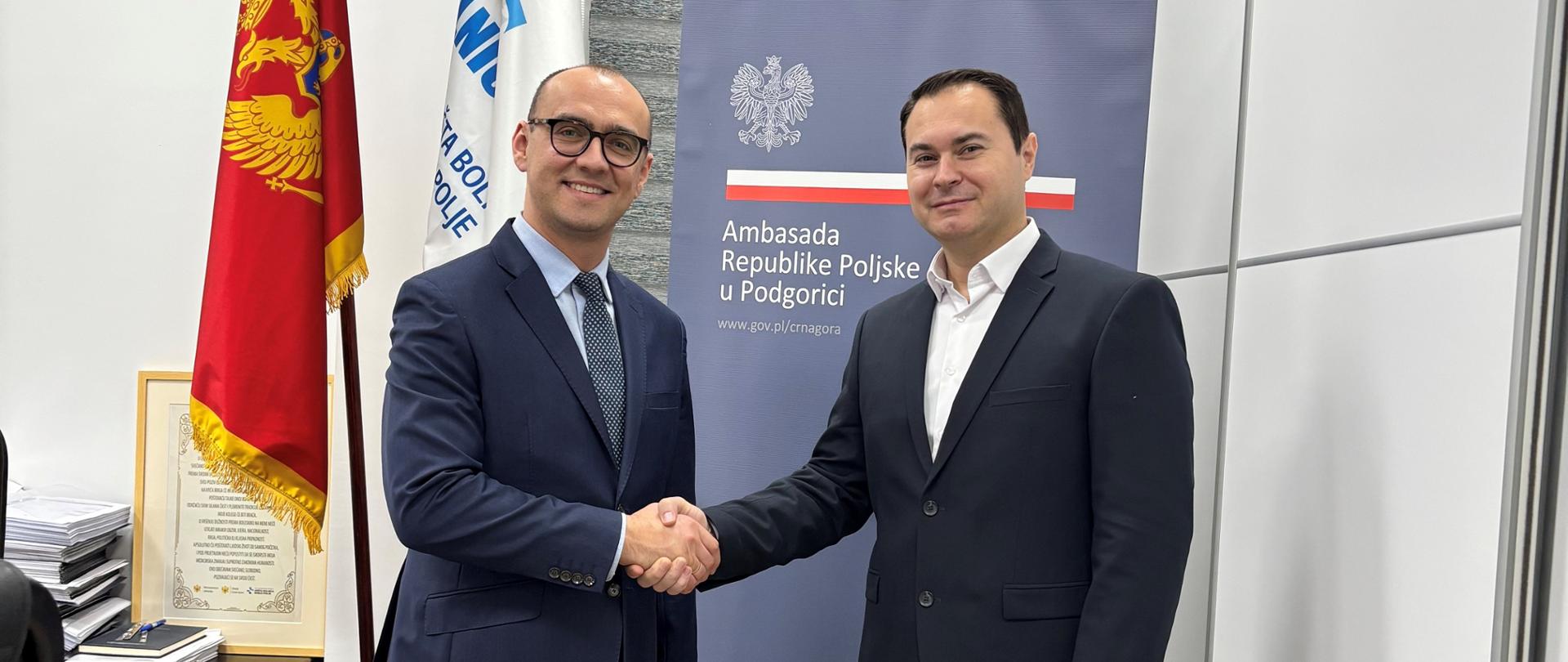 CDA_Bartosz_Marcinkowski_i_dyrektor_Szpitala_Bijelo_Polje_Kenan_Erović podają sobie ręce; w tle flaga Czarnogóry, Miasta Bijelo Polje i baner z napisem Ambasada RP w Podgoricy