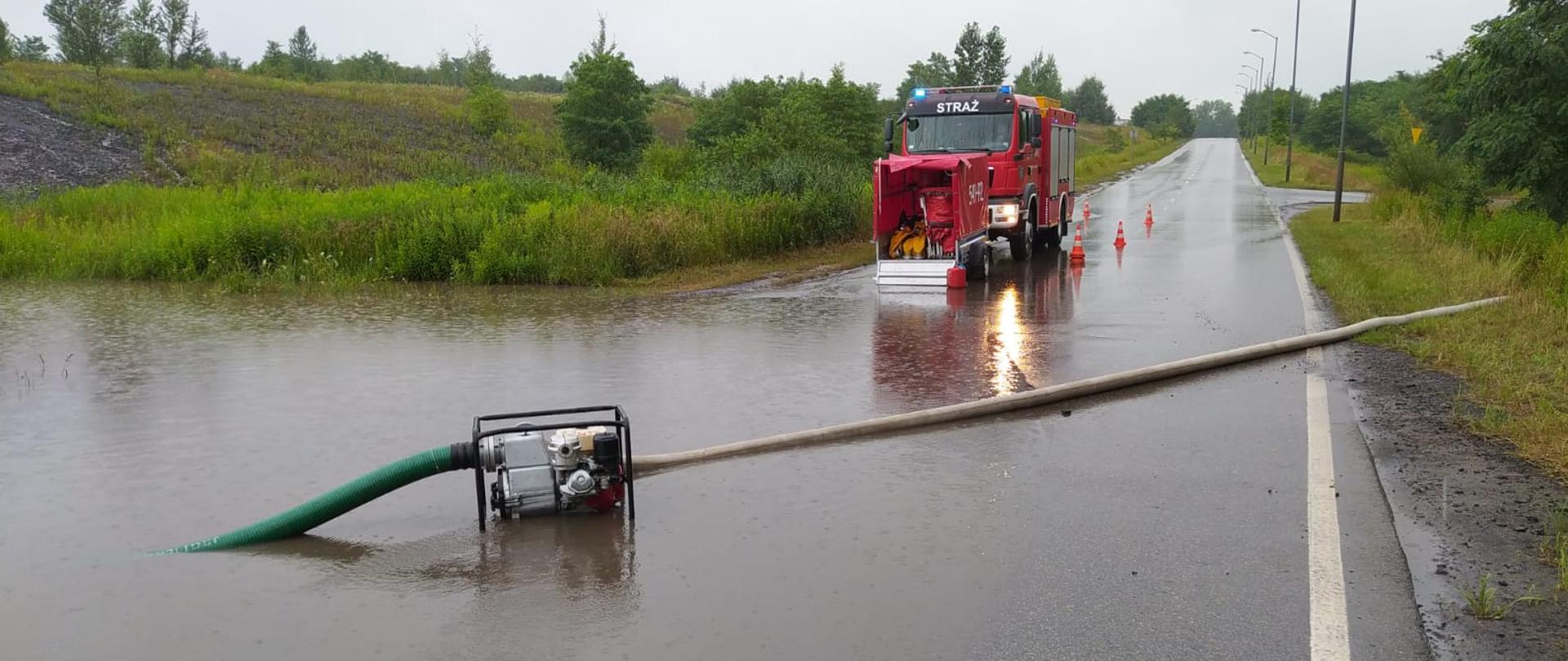 Zalana po ulewach droga, samochód strażacki ze sprzętem, pompa ustawiona do wypompowywania wody