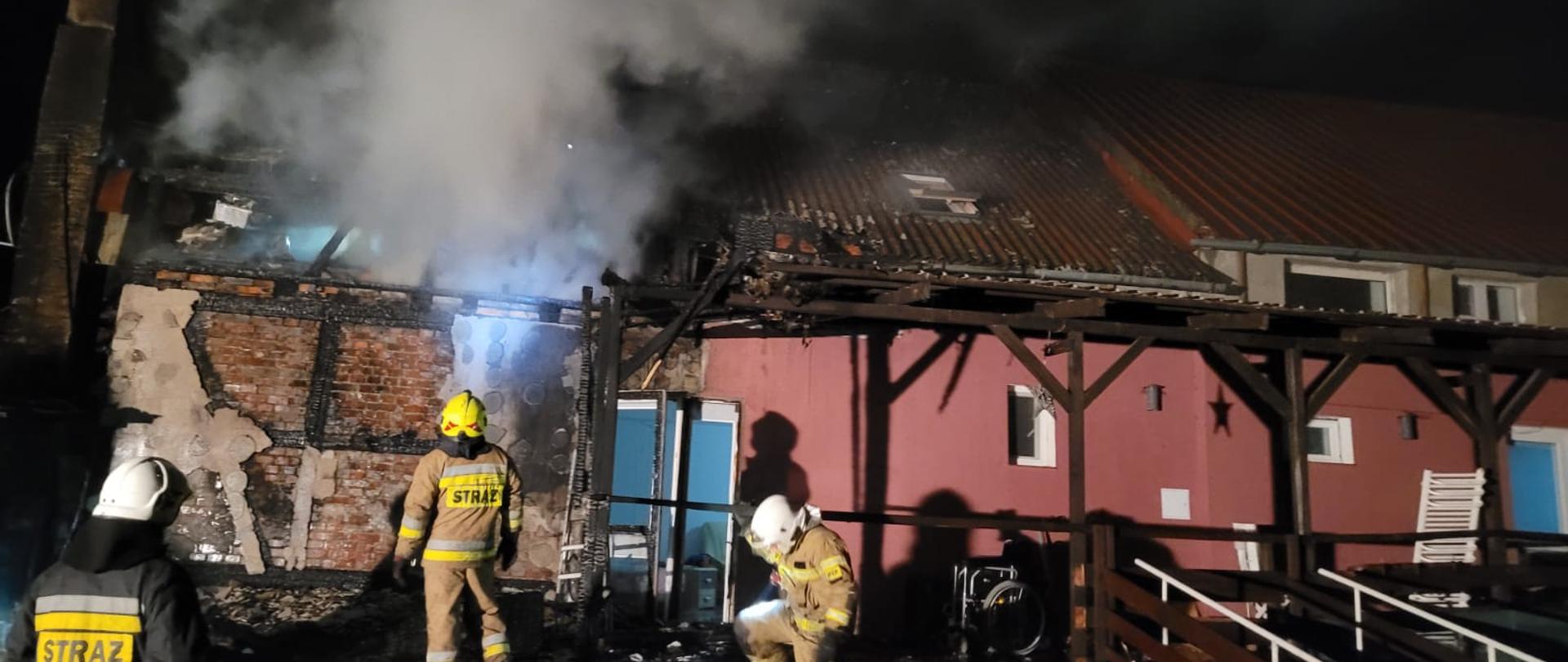 Strażacy stoją przed budynkiem w którym rozwijał się pożar