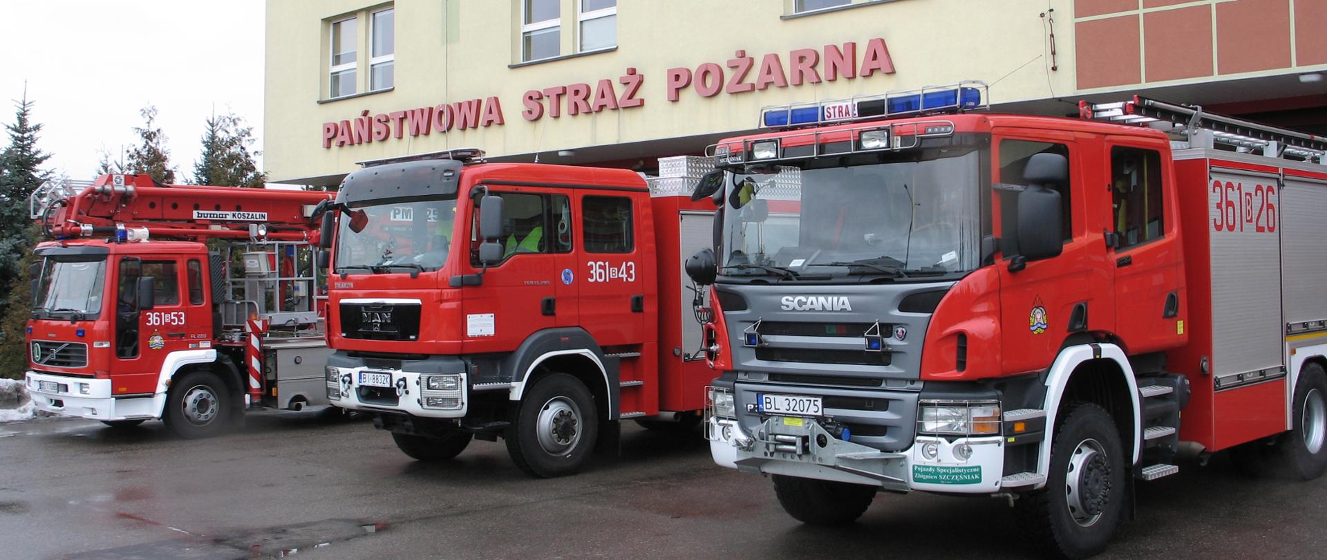 Na tle budynku Komendy Miejskiej Państwowej Straży Pożarnej w Łomży widoczne są trzy pojazdy będące w potencjale tutejszej komendy. Pojazdy są ustawione w rzędzie
w następującej kolejności: dwa pierwsze pojazdy są samochodami ratowniczo-gaśniczymi, natomiast trzeci, a zarazem ostatni z nich to samochód specjalny z podnośnikiem hydraulicznym.
