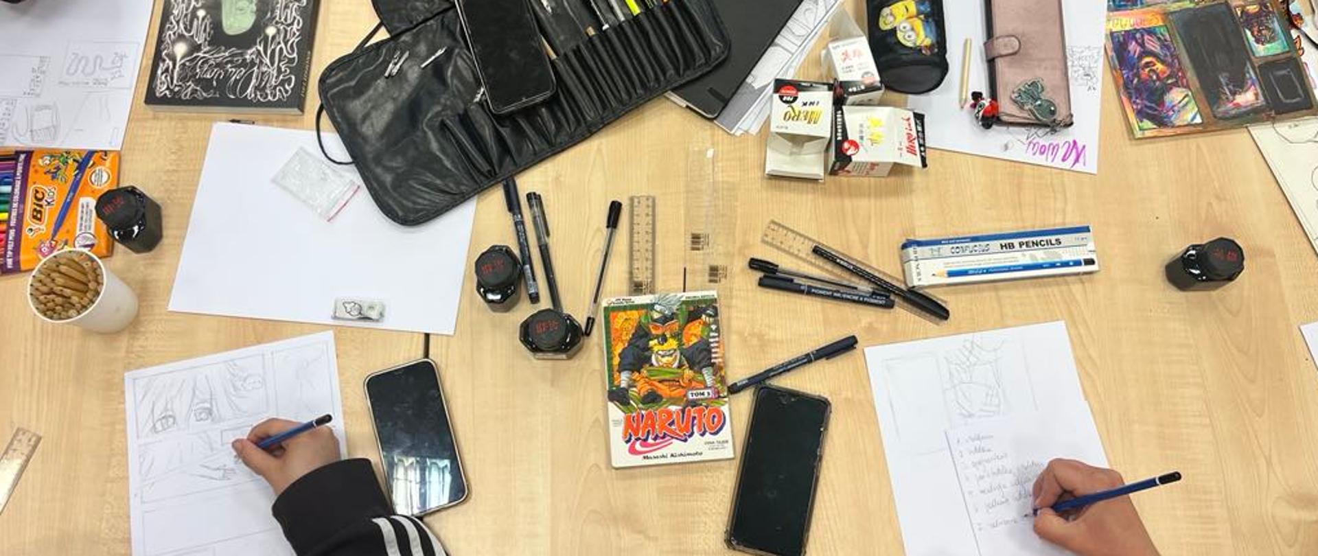 Ujęcie z lotu ptaka na stół z ujęciem rąk w trakcie tworzenia komiksu