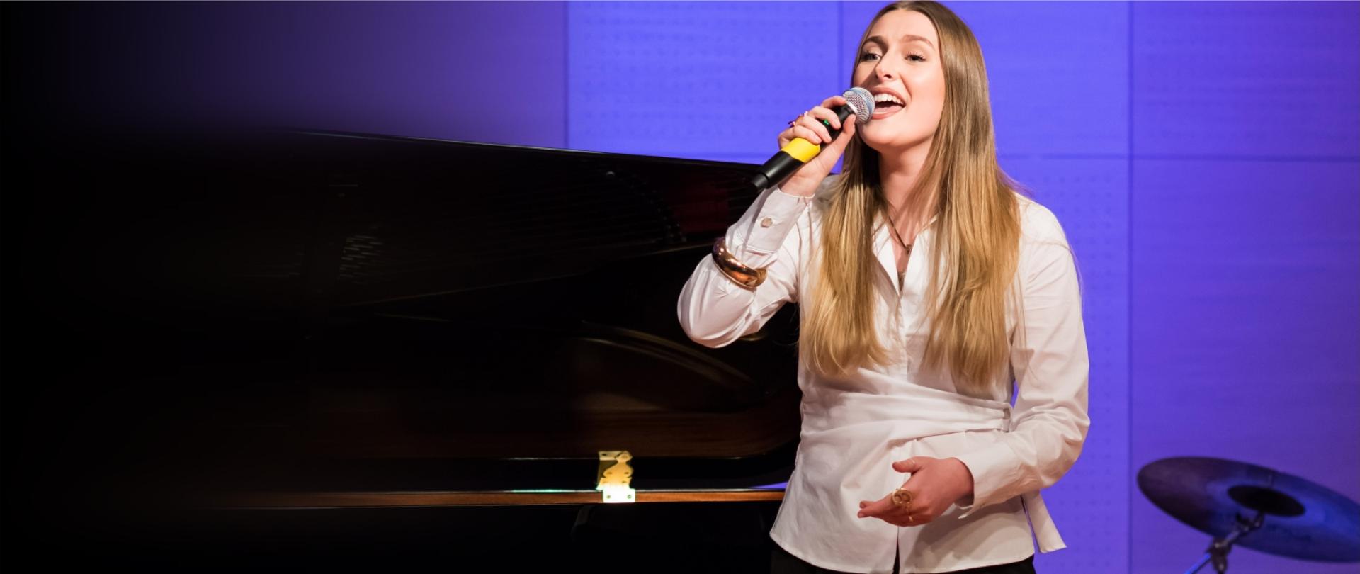 Zdjęcie przedstawia śpiewającą uczennicę ZPSM stojącą przy fortepianie