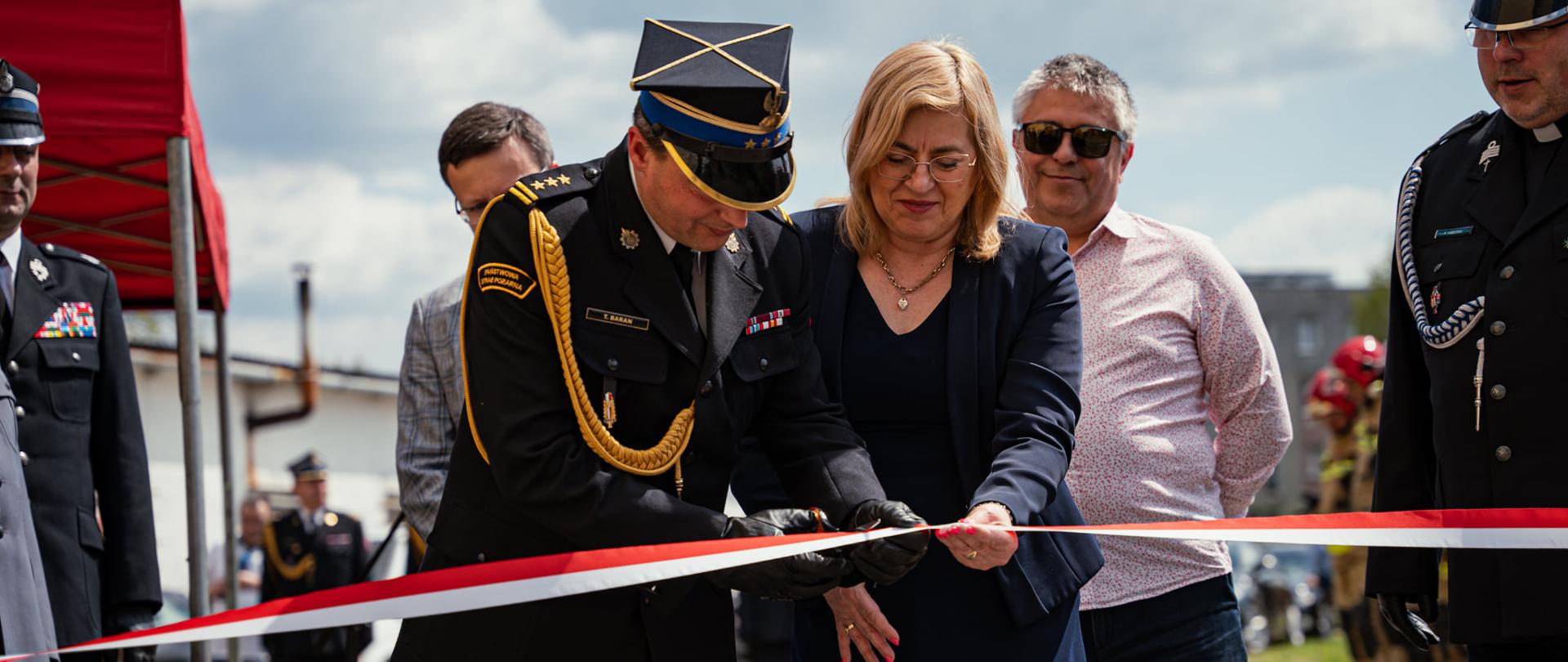 Zdjęcie przedstawia Komendanta Miejskiego PSP w Rzeszowie wraz Panią Wiceprezydent Miasta Rzeszowa podczas symbolicznego otwarcia wystawy pożarniczej - przecinania biało-czerwonej wstęgi nożyczkami.