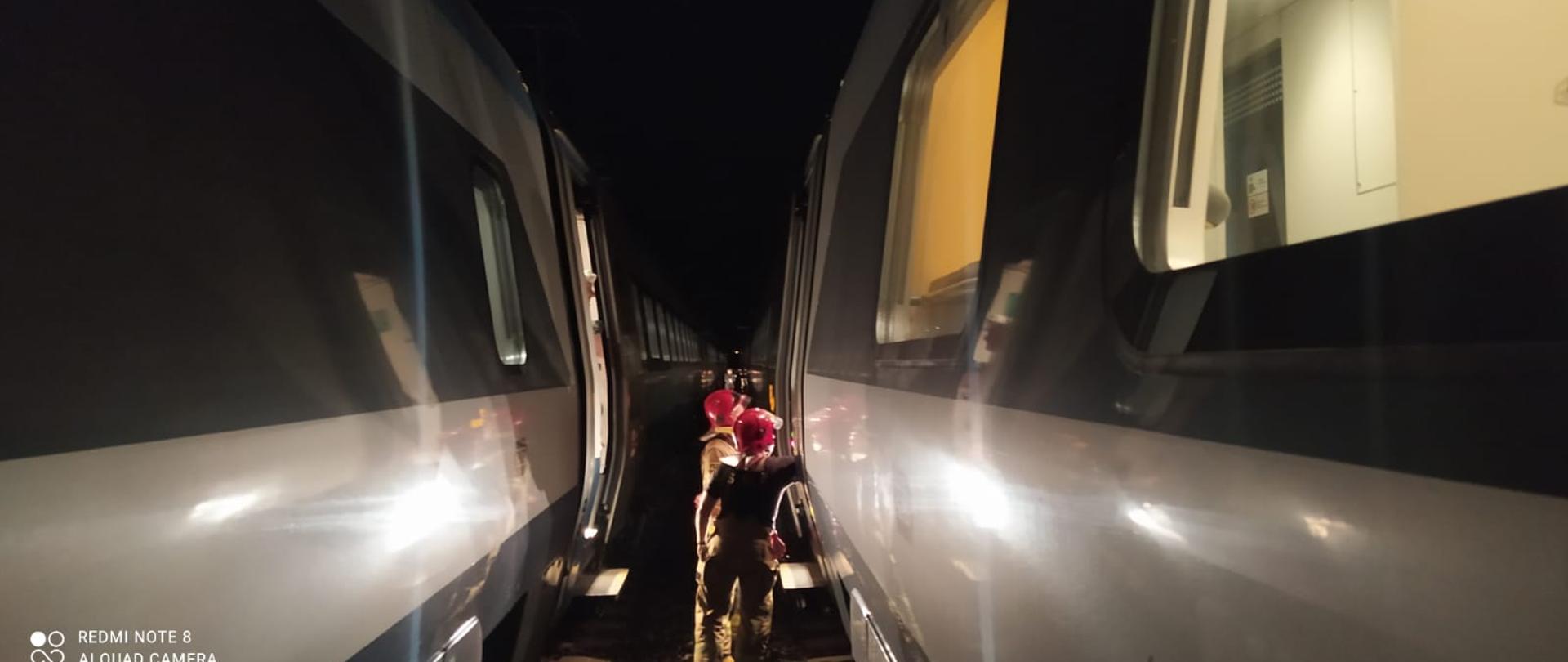 strażacy pomagają przejść pasażerom pociągu ekspresowego do drugiego składu postawionego przez linie kolejowe.