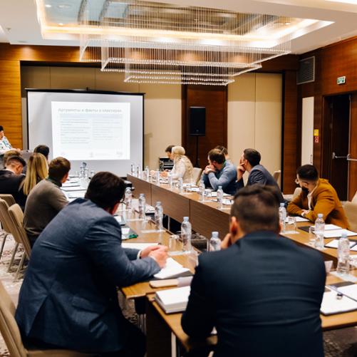 Grupa osób siedzi przy stole konferencyjnym i obserwuje prezentację 