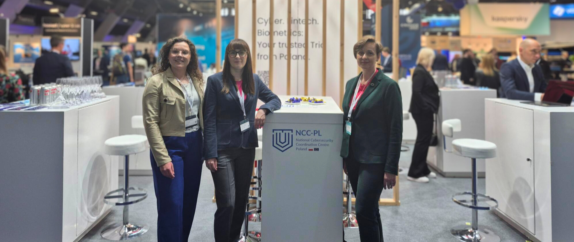 3 przedstawicielki NCC-PL pozujące do zdjęcia przy stanowisku NCC-PL na konferencji Cybersec Europe 2025