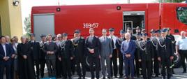 Stojący strażacy oraz wszyscy zaproszenie goście przed samochodem ratowniczo - gaśniczym