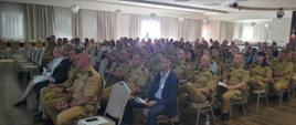 Zdjęcie przedstawia strażaków oraz osoby cywilne podczas seminarium. Osoby siedzą na krzesełkach na sali , natomiast prelegent omawia temat.