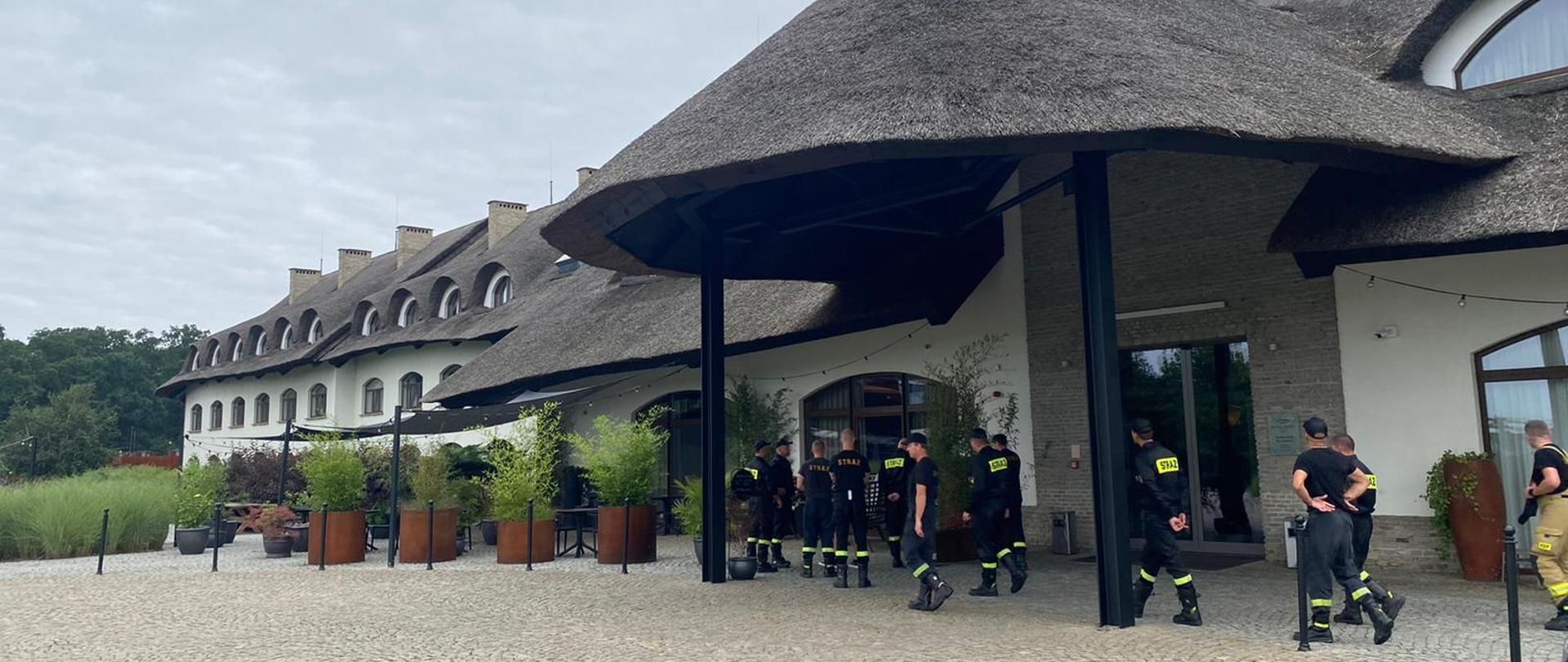 Dzień, strażacy na tle wejścia głównego hotelu.