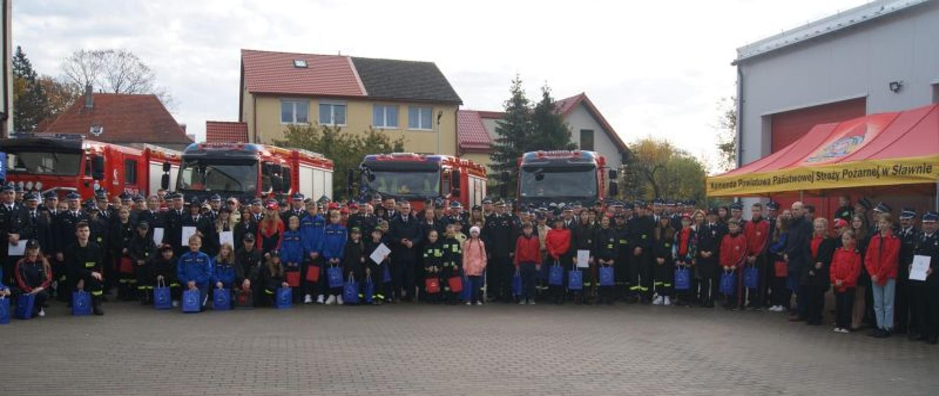 Zdjęcie grupowe wszystkich osób uczestniczących w przekazaniu promes.Wszyscy stoją blisko siebie. W tle niebo. Na zdjęciu są osoby w mundurach, kobiety, dzieci, osoby ubrane w cywilne ubrania.