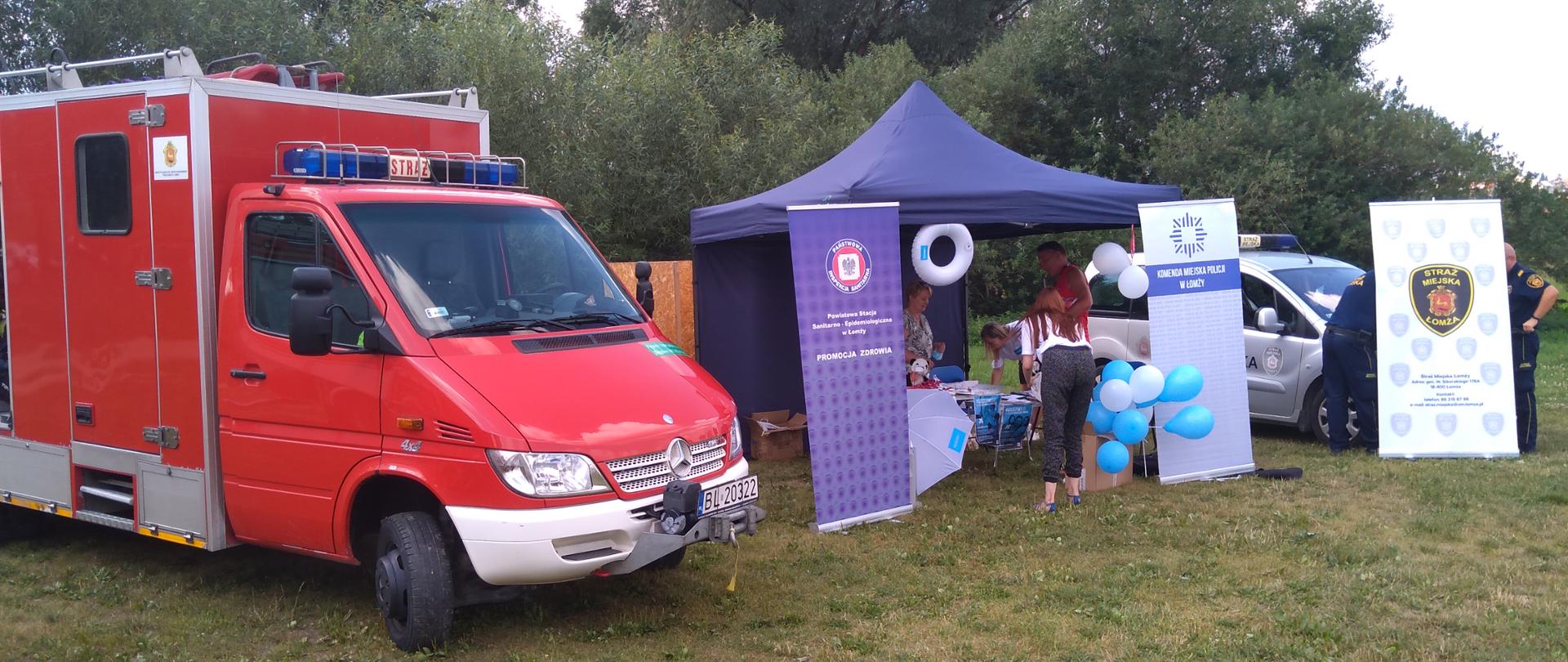 Na zdjęciu samochód ratownictwa wodno-nurkowego Komendy Miejskiej Państwowej Straży Pożarnej w Łomży który stoi przy stanowisku Sanepidu , Policji i Straży Miejskiej w Łomży . W namiocie osoby zainteresowane uzyskuje odpowiedzi na temat szczepień przeciwko Covid-19. 