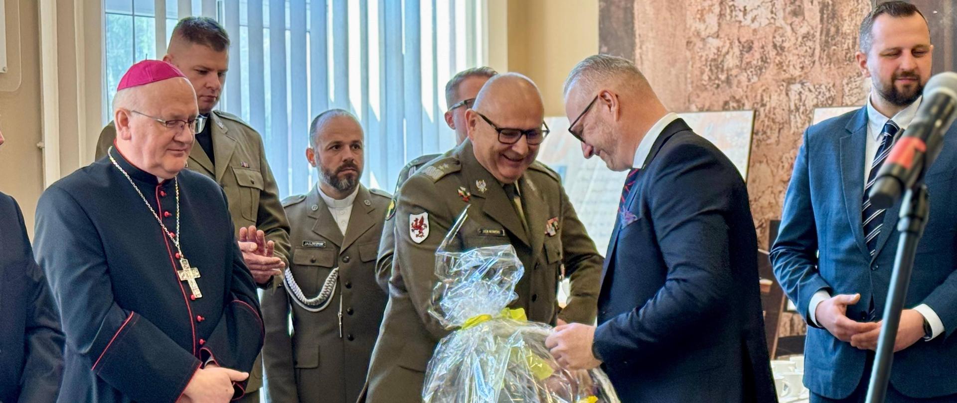 Mężczyzna w garniturze przekazuje kosz prezentowy mężczyźnie w mundurze 