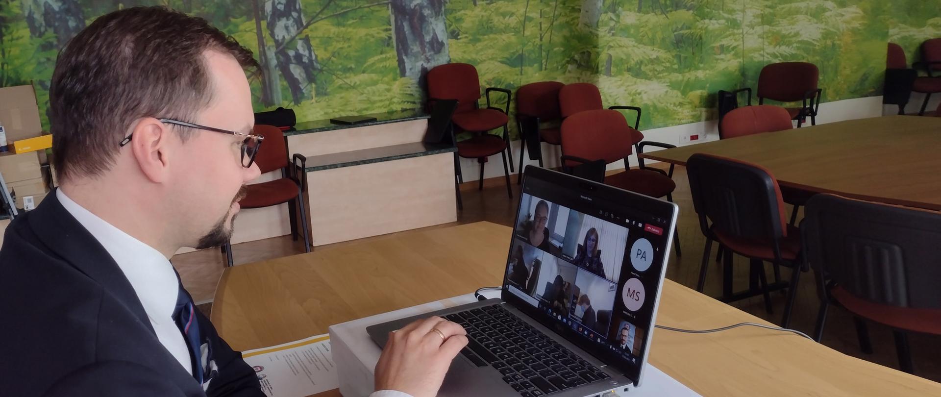 mężczyzna w okularach siedzi przed otwartym laptopem a na monitorze wyświetlone są sylwestki innych uczestników konferencji