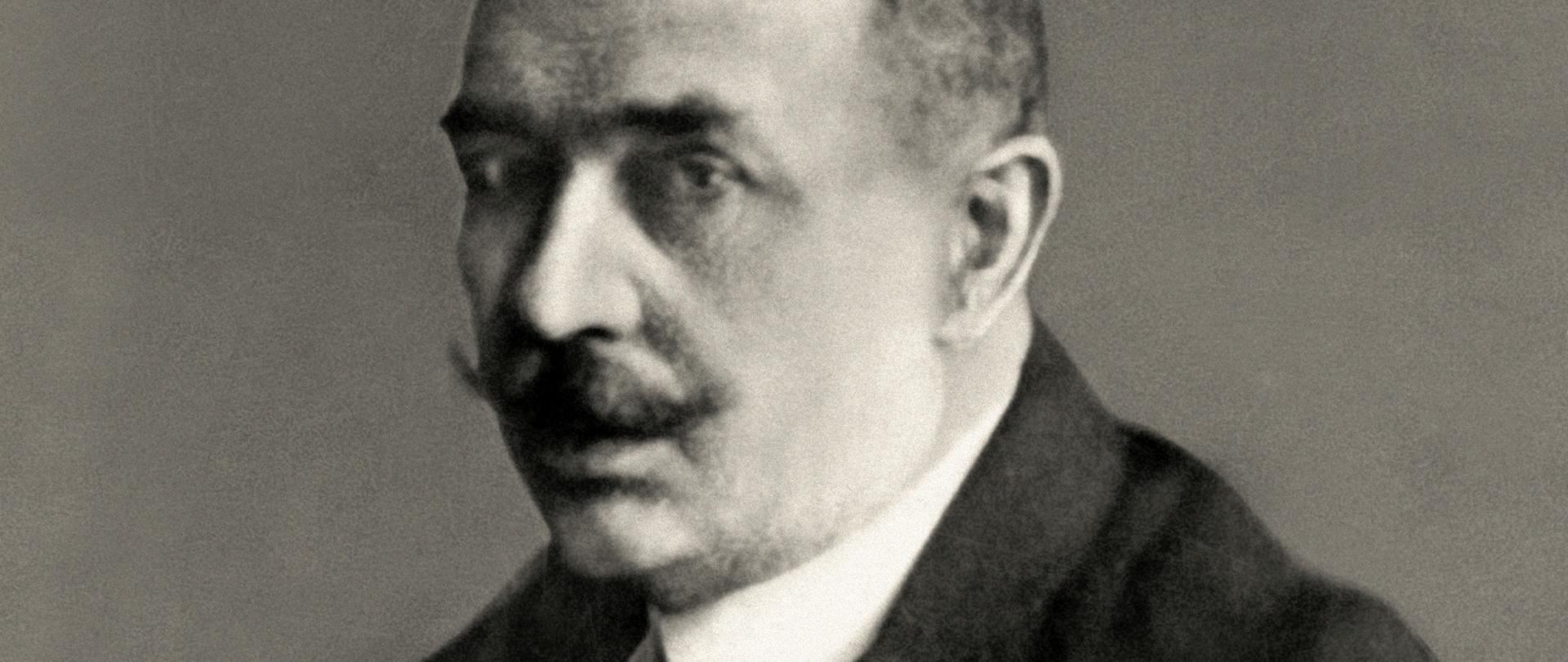 Maurycy Zamoyski - półprofil mężczyzny z bujnym wąsem, ciemnymi włosami, ciemna marynarka, ciemny krawat, biała koszula.