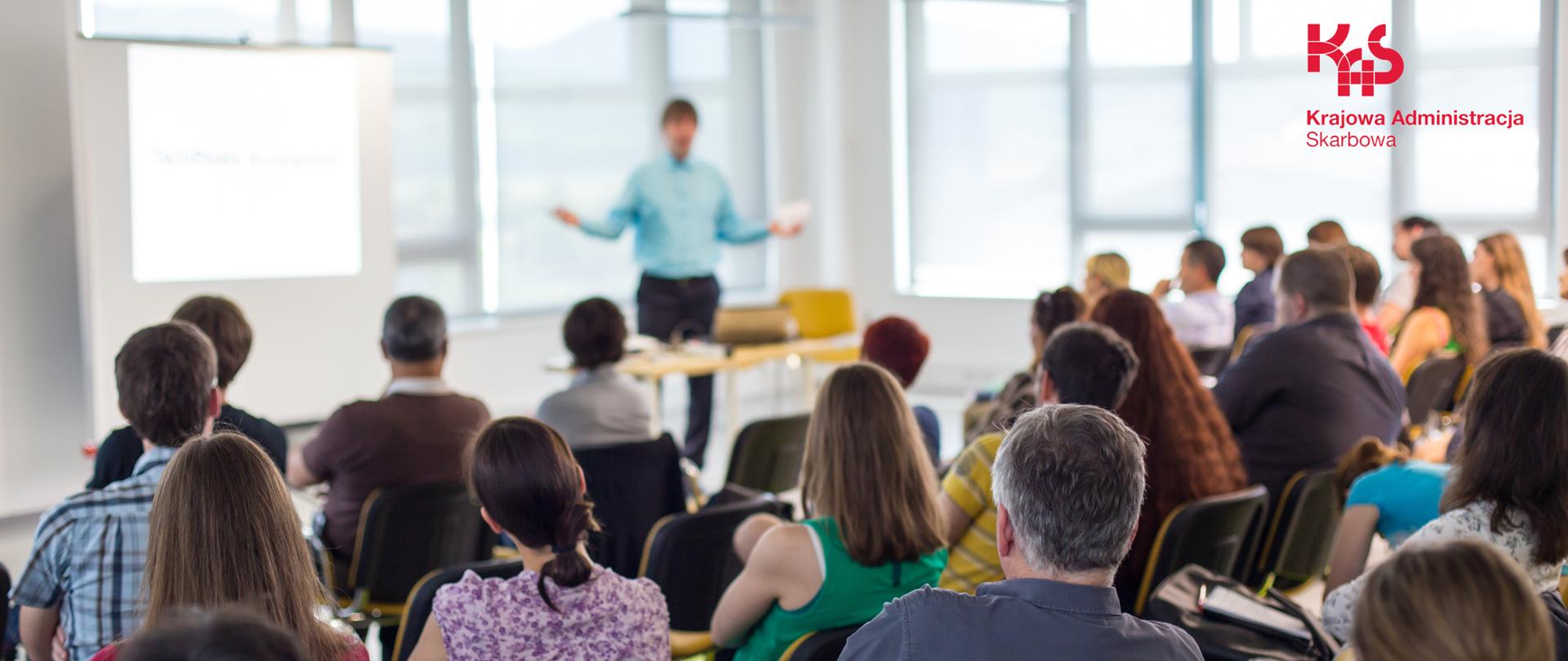 Spotkanie informacyjne, wykładowca prowadzi spotkanie, osoby słuchające wykładu.