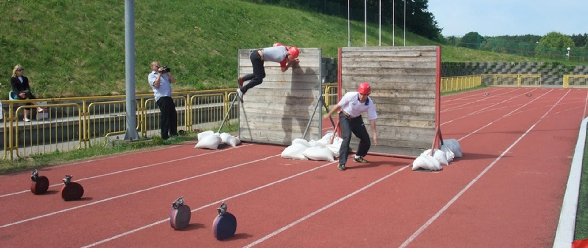 Zdjęcie przedstawia zawodników podczas pożarniczego toru przeszkód