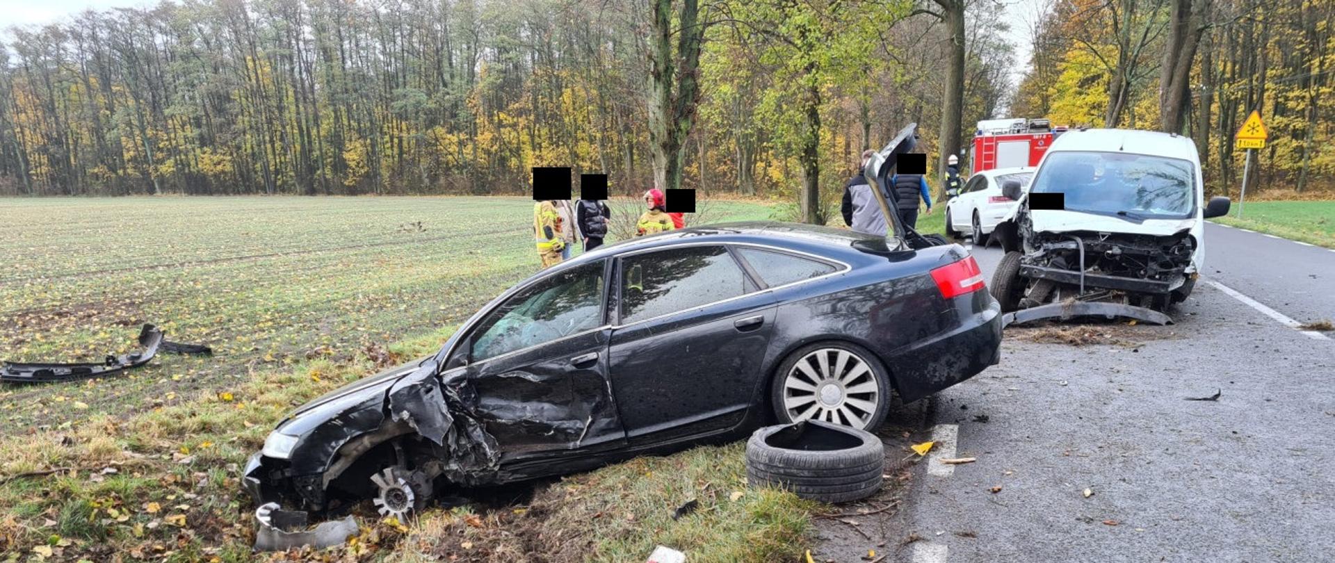 Uszkodzona lewa strona czarnego samochodu, brak koła, samochód w rowie, za nim uszkodzony biały samochód