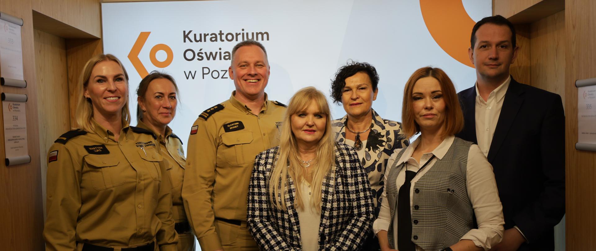 zdjęcie grupowe strażacy, trzy kobiety oraz mężczyzna, w tle napis kuratorium oświaty w Poznaniu