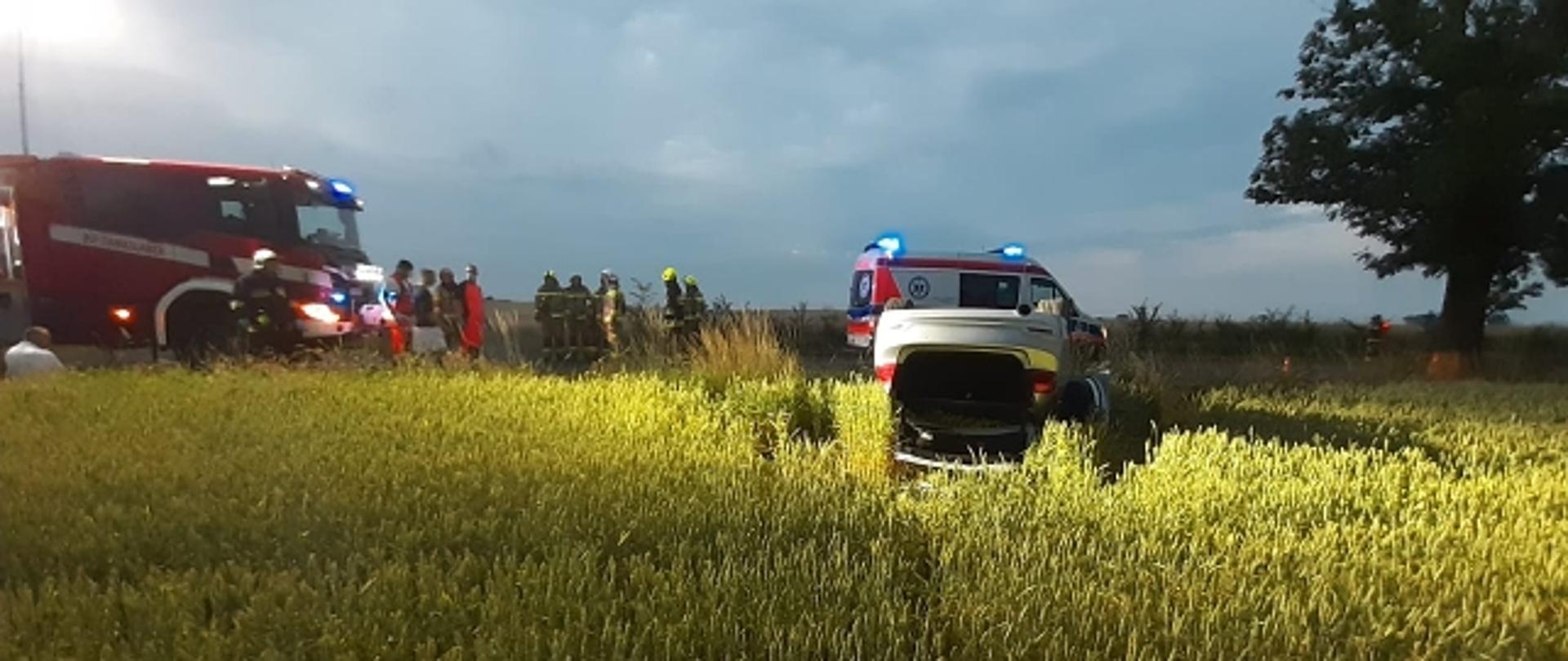 Na zdjęciu widać auto w polu oraz wóz strażacki