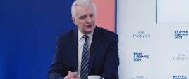 Wicepremier, minister rozwoju, pracy i technologii Jarosław Gowin siedzący przy stole, za jego plecami banner Polityka Insight