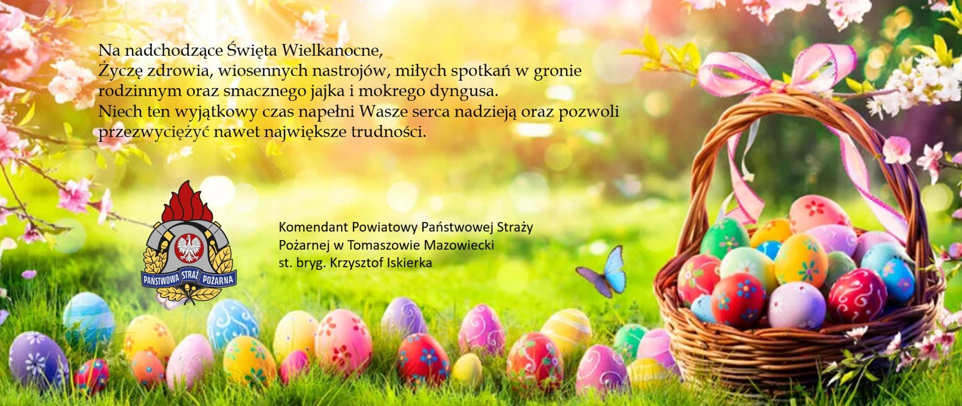 Grafika przedstawiająca koszyczek z pisankami położony na trawie. Na grafice napisane są życzenia: "Na nadchodzące Święta Wielkanocne, Życzę zdrowia, wiosennych nastrojów, miłych spotkań w gronie rodzinnym oraz smacznego jajka i mokrego dyngusa. Niech ten wyjątkowy czas napełni Wasze serca nadzieją oraz pozwoli przezwyciężyć nawet największe trudności". Życzenia składa Komendant Powiatowy Państwowej Straży Pożarnej w Tomaszowie Mazowieckim starszy brygadier Krzysztof Iskierka.
