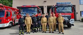Strażacy pozują do zdjęcia grupowego na tle samochodów pożarniczych