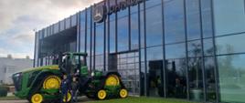 Dwaj mężczyźni stoją na tle nowoczesnej maszyny rolniczej przed siedzibą firmy John Deere.