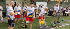 Grupa ludzi ćwiczy z kettlami w sportowych koszulkach, jeden z mężczyzn ma protezę nogi