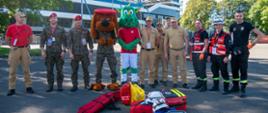 Grupa uczestników zawodów, w tym strażacy PSP, żołnierze oraz maskotki, stojąca wspólnie na placu przed stadionem w Krakowie. Na pierwszym planie widoczne torby medyczne i kaski ratownicze.
fot. Michał Mizia