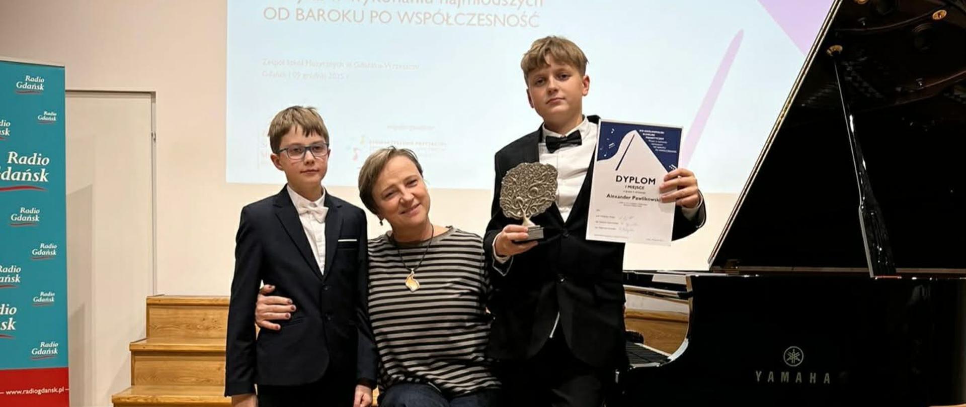 Przy fortepianie w szkole muzycznej w Gdańsku-Wrzeszczu pozuje Elżbieta Lieder wraz z uczniami biorącymi udział w konkursie.