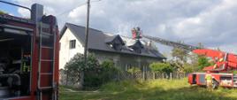Zdjęcie przedstawia drabinę strażacką oraz strażaków gaszących dach budynku mieszkalnego. 