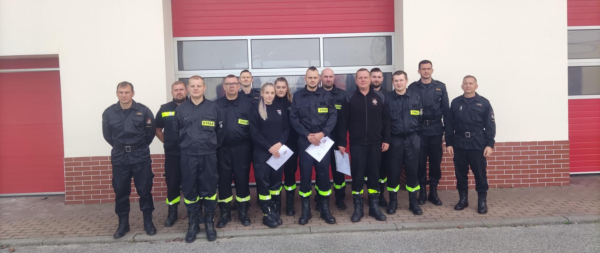 Zdjęcie przedstawia absolwentów szkolenia kierujących działaniem ratowniczym (dowódców OSP) na tle strażnicy Komendy Powiatowej Państwowej Straży Pożarnej w Radziejowie. 