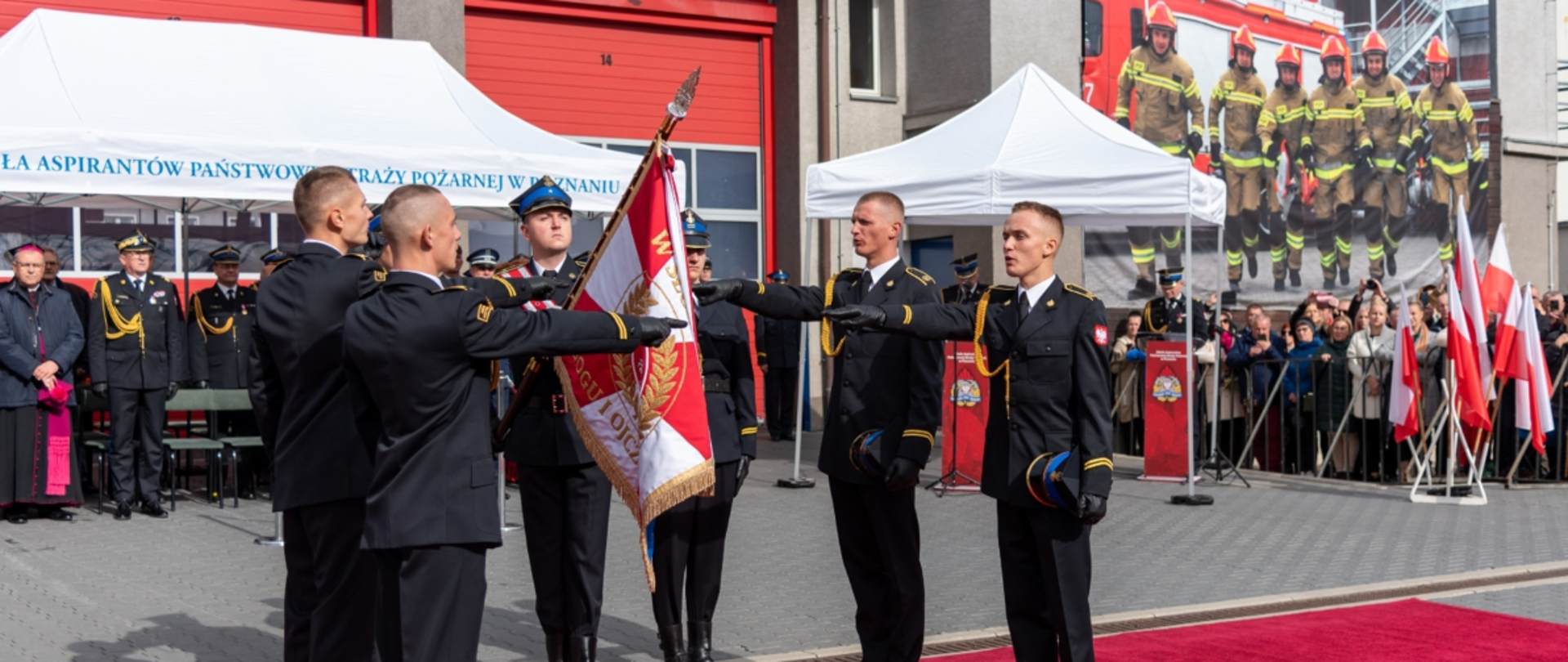 ślubowanie słuchaczy sa psp w poznaiu, czterech strażaków stoi przed sztandarem w tle grupa ludzi