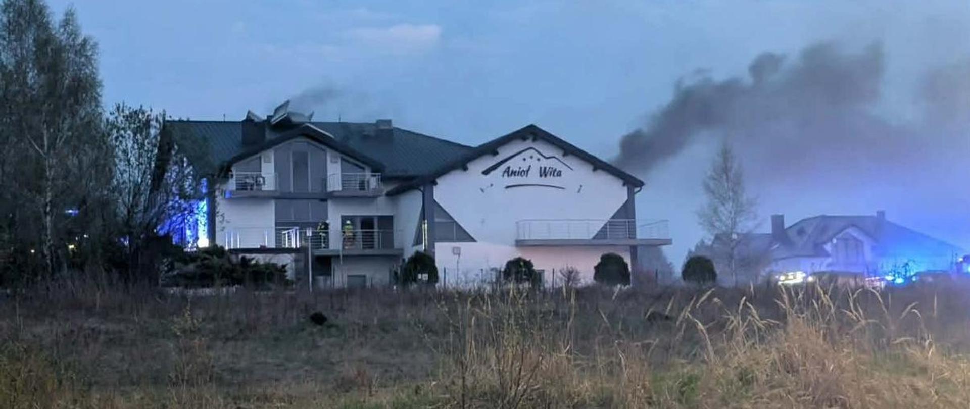 Fotografia przedstawia budynek w którym powstał pożar. Z dachu unosi się gęsty dym.