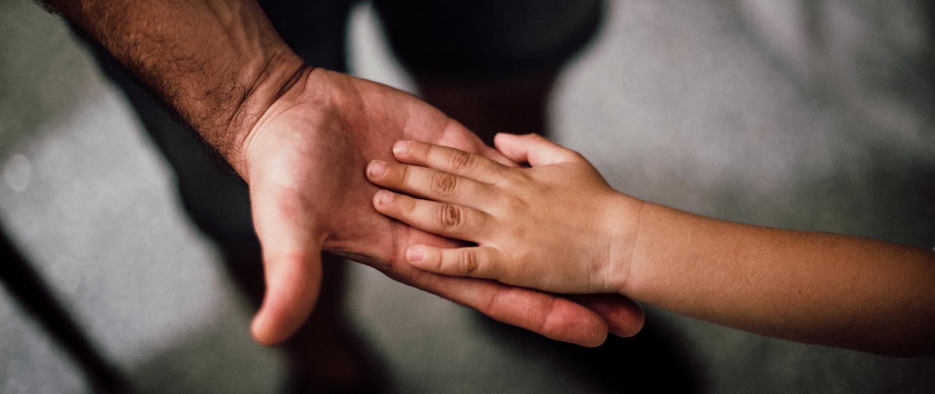 Dłoń dziecka położona na dłoni osoby dorosłej