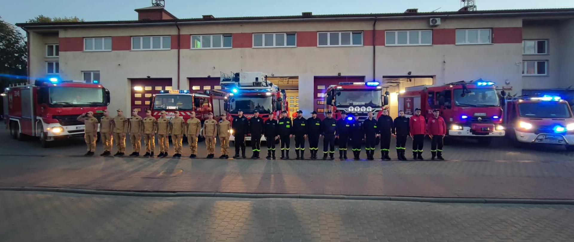 zbiórka strażaków w szeregu przed budynkiem JRG2 w Bydgoszczy, za strażakami stoi 6 samochodów pożarniczych