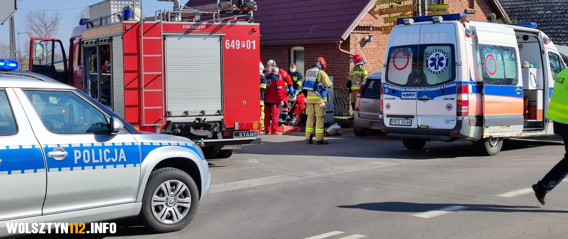 Radiowóz policyjny, wóz strażacki, karetka pogotowia, w tle służby walczą o życie mężczyzny.