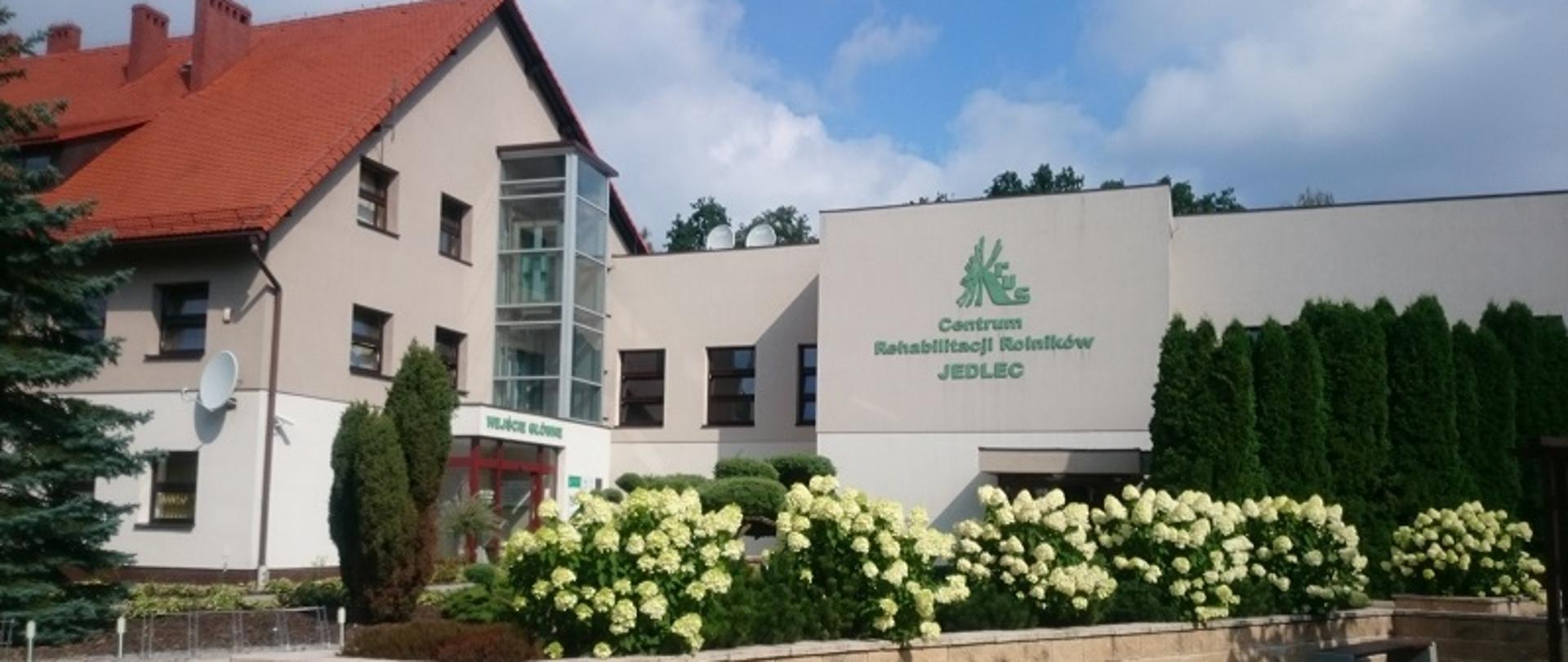 budynek CRR KRUS w Jedlcu z kwitnącymi białymi kwiatami na klombach przed wejściem