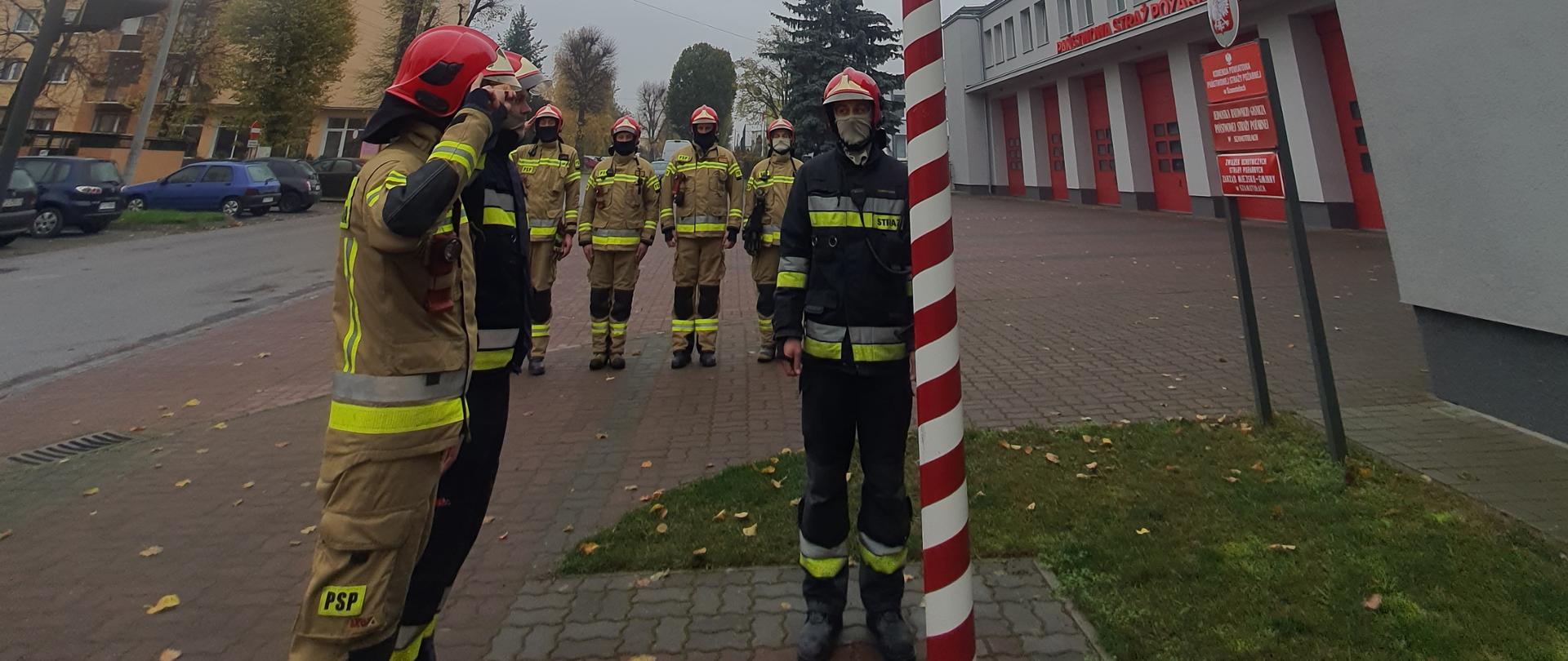 Siedmiu strażaków podczas podnoszenia flagi państwowej przed budynkiem Komendy Straży
