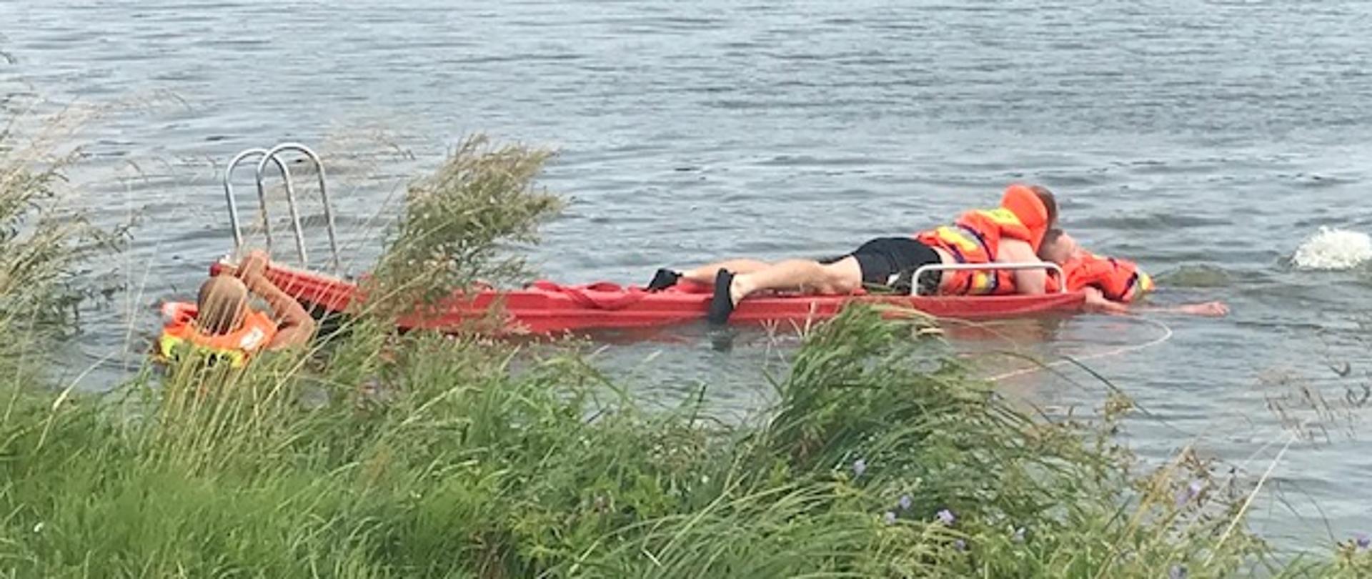 Na zdjeciu widoczni ratownicy holujacy tonącego z uzyciem sań wypornościowych