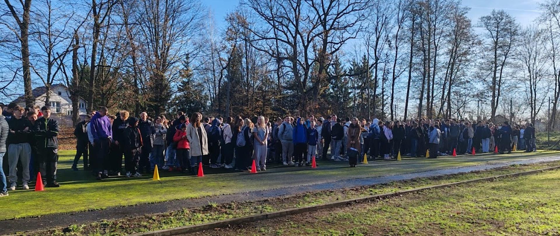 Uczniowie i nauczyciele stojący na miejscu ewakuacji.