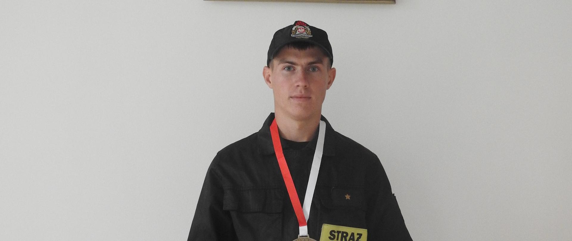 Strażak w rękach trzyma dyplom. Na szyj ma medal. 