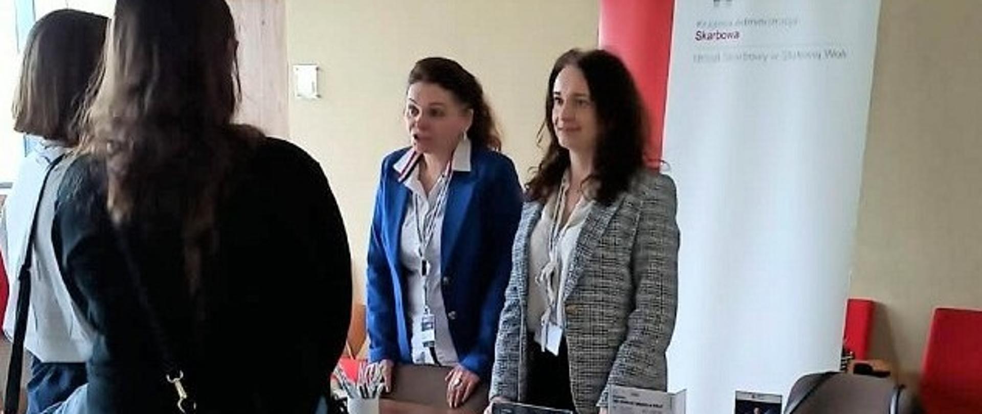 Uczestniczki targów stoją przy stanowisku KAS. Przed nimi są ekspertki KAS. 